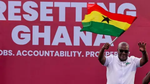 Reuters John Mahama is in the right-hand corner of the picture wearing a white shirt and waving a Ghana flag. Behind him is a large poster that says 'Resetting Ghana'