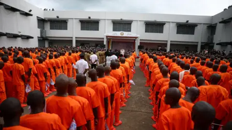 Reuters Dozens of prisoners in orange uniforms line up in front of the Pope, who can be seen in the distance under a shelter