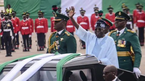 Getty Images Nigeria President Bola Tinubu in a white robe waves his hands during a presidential parade at Eagles square, Abuja - 2024
