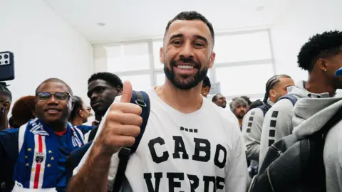 Michel Mvondo/BBC Pico Lopes smiles at the camera, wearing a white t-shirt emblazoned with the words "Cabo Verde"