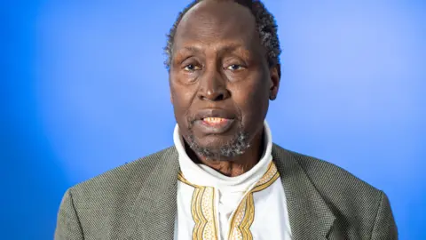 Getty Images The late Kenyan write Ngũgĩ wa Thiong'o, in a white shirt and grey tweed coat