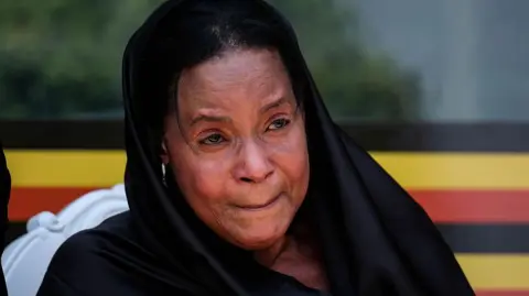 Getty Images Best Kemigisa dressed in black, with a black head covering draped over her shoulders, appearing emotional 