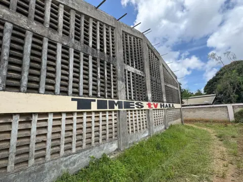 A grey concrete building with lots of air vents in the wall. There is a sign saying Times TV Hall
